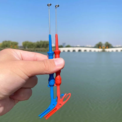 Hand holding red and blue hook remover tools by a lake